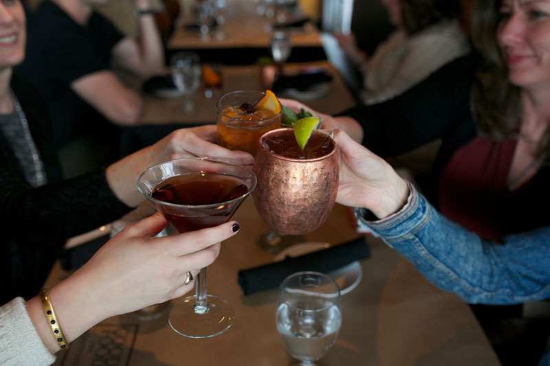 close-up of three people cheersing their cocktail glasses at a restaurant table